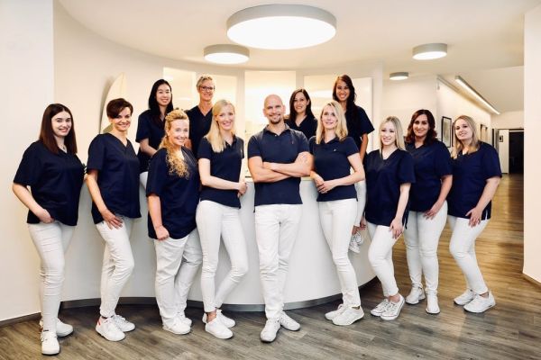 Das Team der Zahnarztpraxis Heitmüller, Hannover List, in einheitlicher Arbeitskleidung vor dem Empfangsbereich der Praxis.