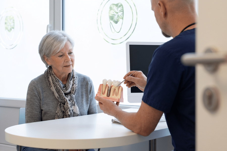 Zahnarzt erklärt einer Patientin anhand eines Kiefermodells den Ablauf einer Zahnimplantat-Behandlung