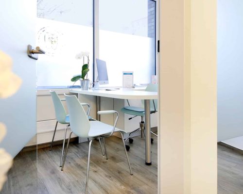Helles und modernes Beratungszimmer der Zahnarztpraxis Heitmüller, Hannover List, mit Schreibtisch, Stühlen, Computer und viel natürlichem Licht.