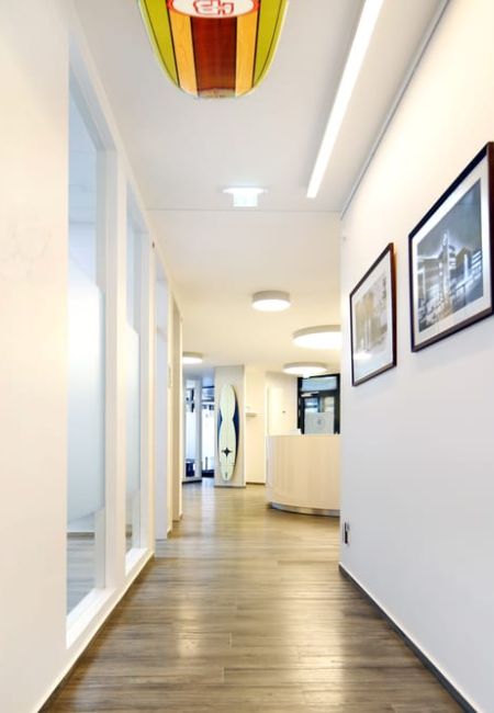 Blick in den Praxisflur. An der Decke hängt ein Surfbrett und an der Wand finden sich Bilder mit Surfmotiven.