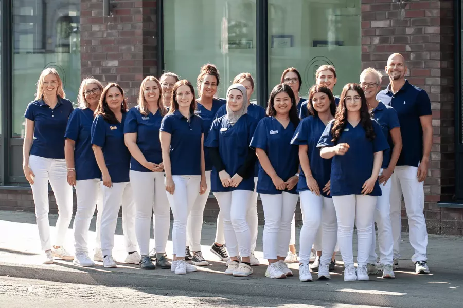 Das Team der Zahnarztpraxis Heitmüller - Hannover List, in blauer und weißer Teamkleidung vor der Praxisfassade.